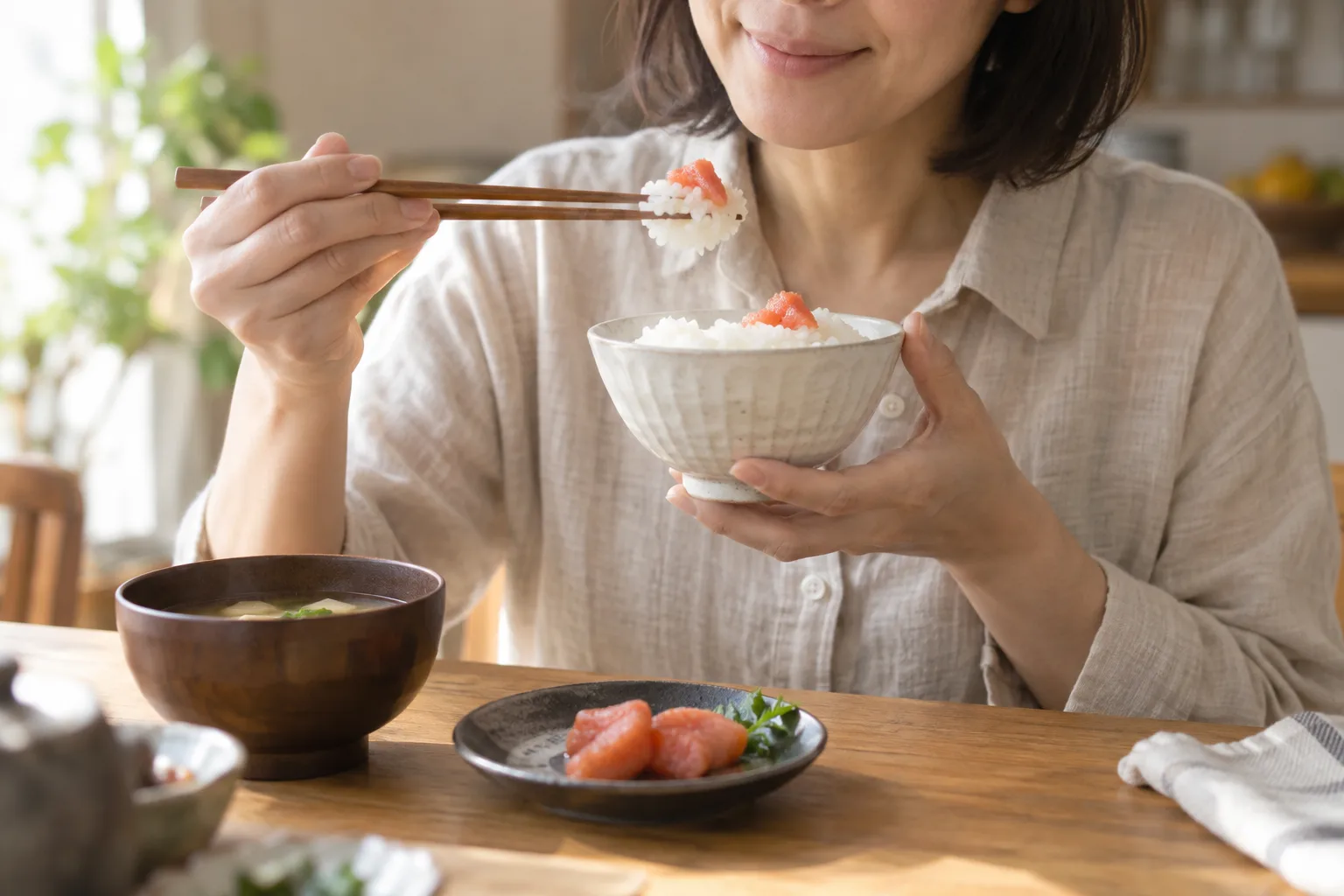 明太子を添えたご飯を、自宅の食卓で味わう女性のイメージ